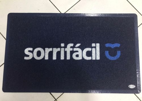 Capacho de porta azul marinho sob medida com a logomarca sorrifácil em branco e ícone de sorriso azul, acabamento com borda de borracha preta, fotografia realista de tapete personalizado sob medida